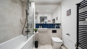 Une salle de bain moderne avec une douche à parois de verre, des toilettes blanches et un lavabo avec un mur de crédence recouvert de carreaux bleus.