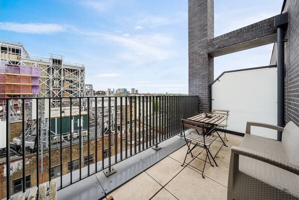 A balcony with a table and chairs, a view of a construction site, and a brick wall.
