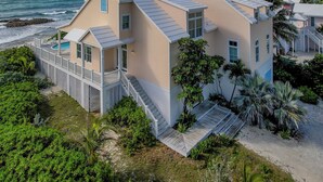 A coastal property with a two-story building, a covered deck, and a staircase leading to the upper level. - Cheers - Your Perfect Beachfront Escape with Private Dock Slip Pool Ocean (Hope Town)
