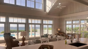 A spacious living area with large windows, a ceiling fan, a pool view, and a kitchen island. - Cheers - Your Perfect Beachfront Escape with Private Dock Slip Pool Ocean (Hope Town)