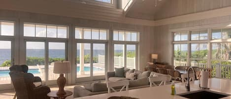 Amplia sala de estar con ventanas grandes, ventilador de techo, vista a la piscina y una isla en la cocina.