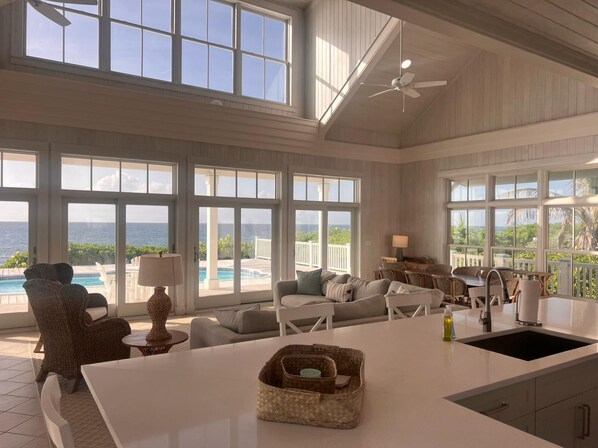 A spacious living area with large windows, a ceiling fan, a pool view, and a kitchen island.