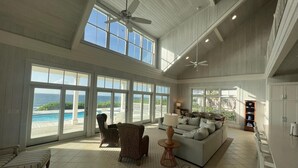 A spacious living room with large windows, a ceiling fan, and a view of the ocean. - Cheers - Your Perfect Beachfront Escape with Private Dock Slip Pool Ocean (Hope Town)