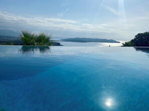 Piscina infinita azul cristalina con vistas al mar y montañas lejanas.