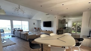 Amplia sala de estar con una gran mesa de comedor, cocina y una zona de estar con vistas al exterior.