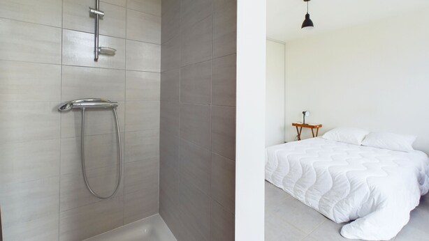 Ein modernes Badezimmer mit Dusche, Toilette und einem Bett mit weißer Bettdecke.