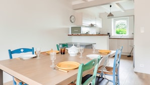 A dining area with a wooden table set for four, chairs, and a kitchen in the background. - Seaview, house for 7 Golfe du Morbihan (Sarzeau)