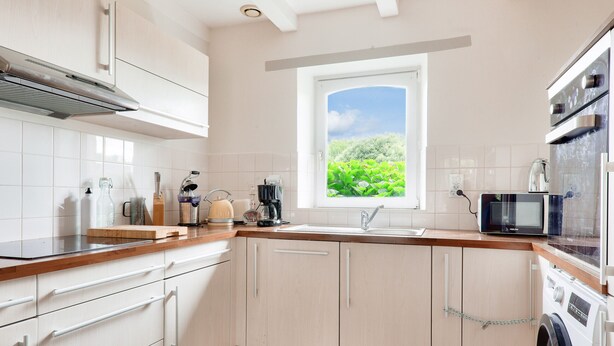 A modern kitchen with white cabinetry, a wooden countertop, a built-in oven, a microwave, and a window with a view of greenery. - Seaview, house for 7 Golfe du Morbihan (Sarzeau)