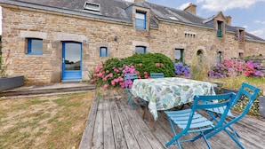 A stone building with a wooden deck, a table with chairs, and a variety of flowers in the garden. - Seaview, house for 7 Golfe du Morbihan (Sarzeau)