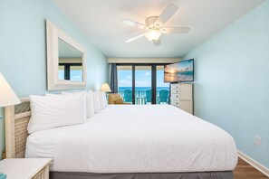 Une chambre d’hôtel avec un grand lit, un ventilateur de plafond, une télévision et une vue sur l’océan par les fenêtres.