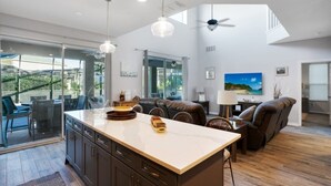 A modern kitchen with a large island, dining area with a sofa, and a TV on the wall.