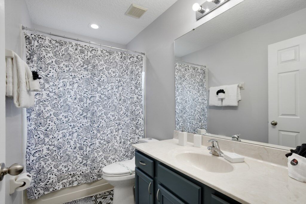 A bathroom with a patterned shower curtain, a toilet, a sink with a mirror, and a door.
