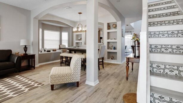A spacious living area with a dining table, a sofa, and a patterned ottoman.