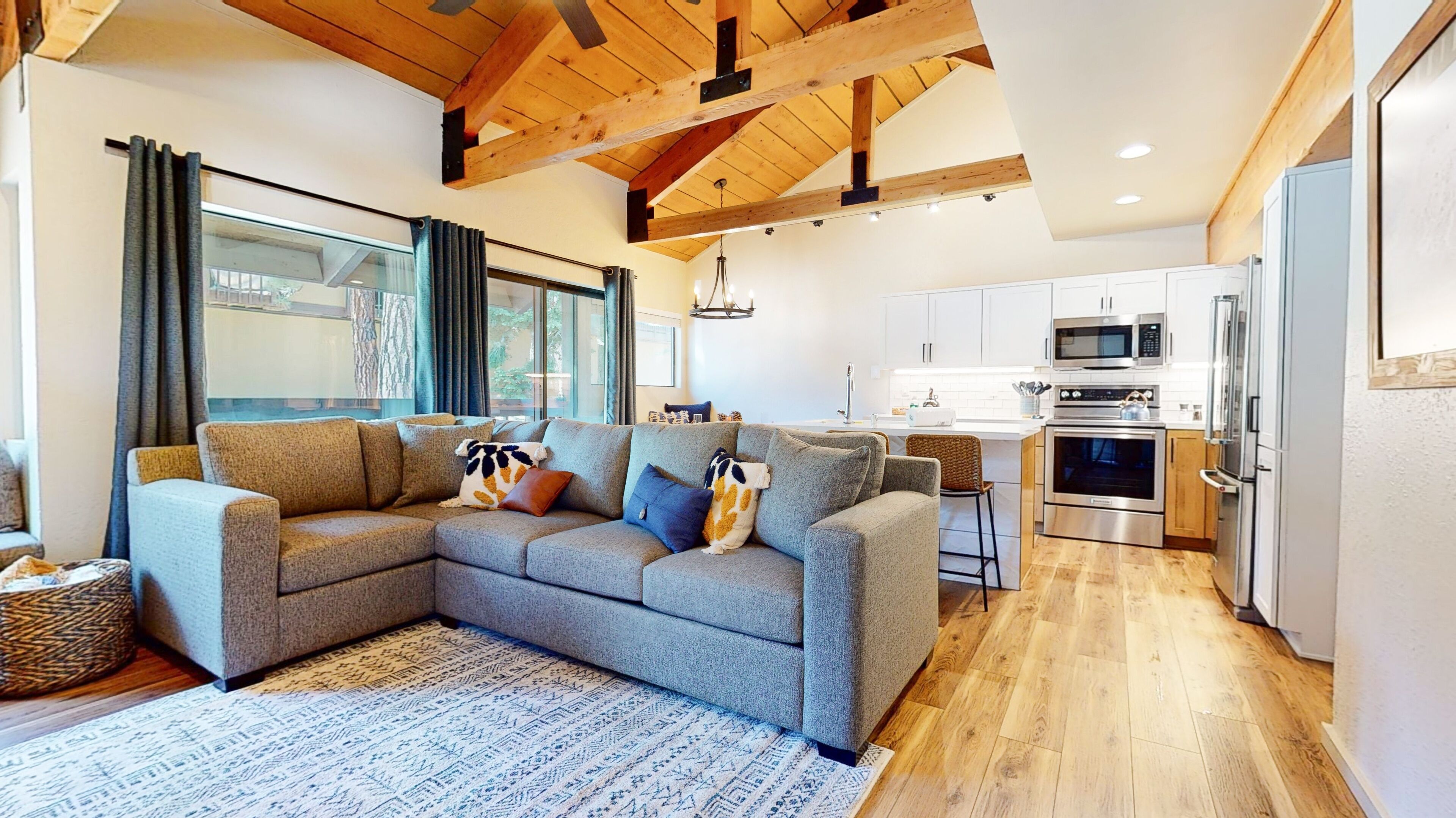 A modern living room with a grey sectional sofa, a patterned rug, and a wooden ceiling.