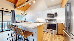 A modern kitchen with a central island, stainless steel appliances, and a wooden ceiling. - Bigwood #45 2 Bedroom Condo by RedAwning (Mammoth Lakes)
