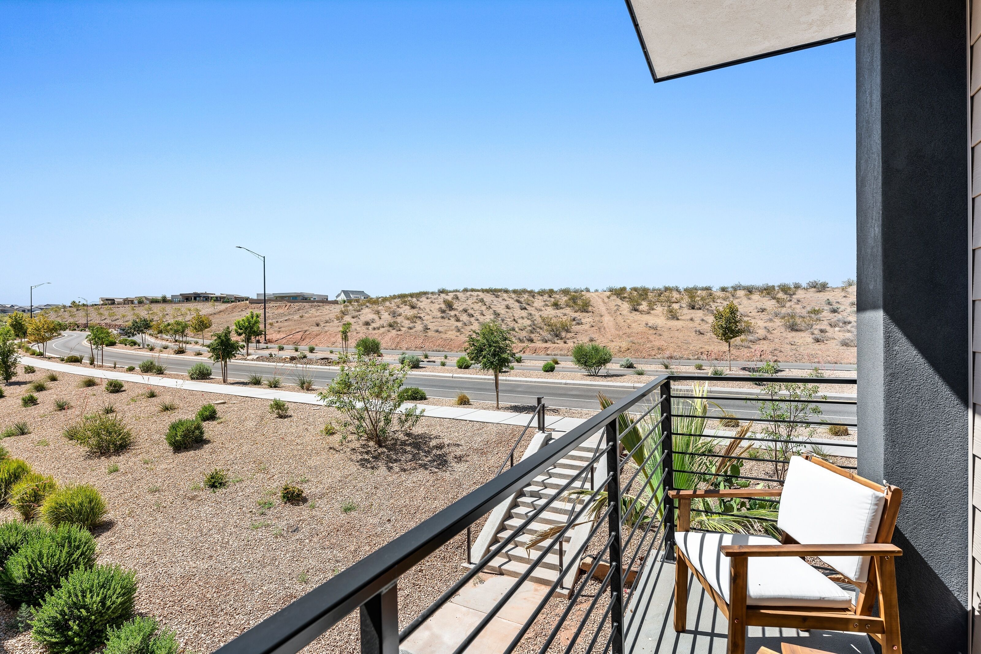 A balcony with a wooden chair and a view of a desert landscape with sparse vegetation and a road.