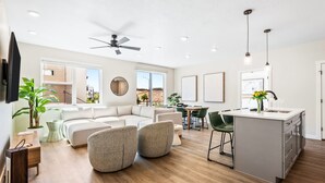 Ein modernes Wohnzimmer mit einer Couch, Sesseln, einem Essbereich und einer Kücheninsel.
