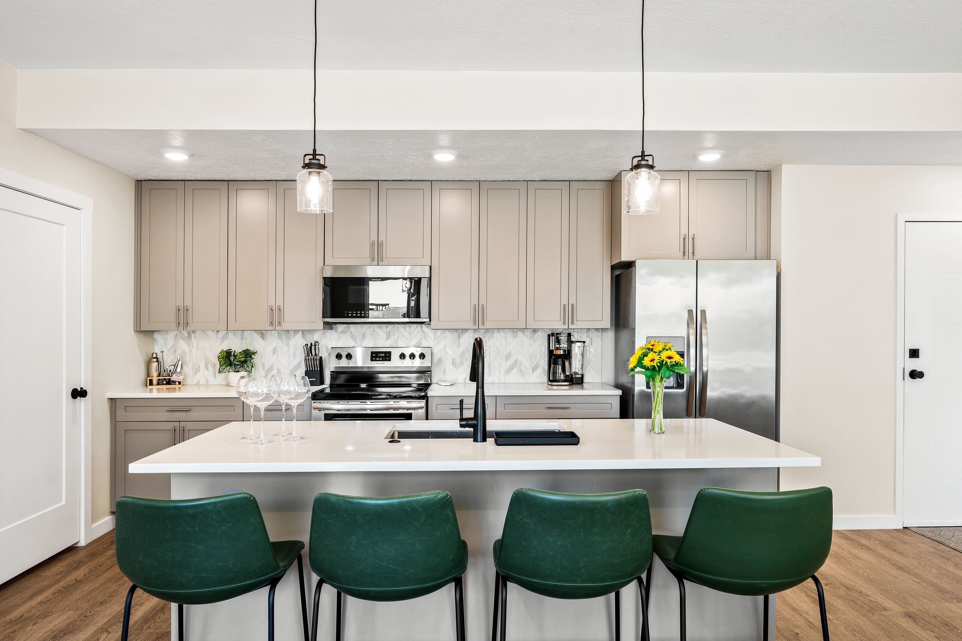 A modern kitchen with a central island, stainless steel appliances, and green chairs.
