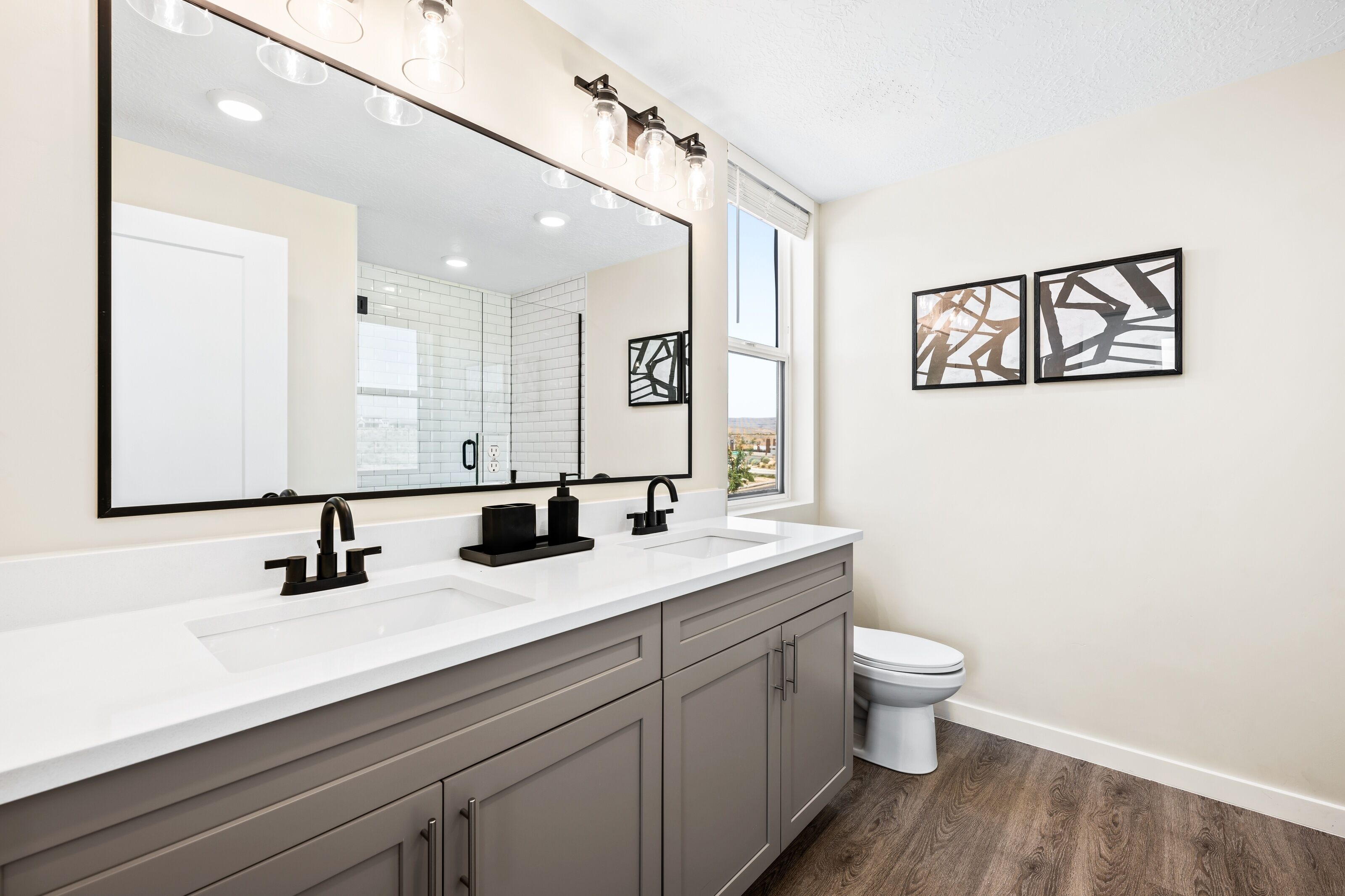 Une salle de bain moderne avec un grand miroir, deux lavabos et des toilettes.