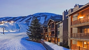 A snow-covered street with a wooden building featuring balconies and a ski lift in the background. - Snow Flower 068 3 Bedroom Condo by RedAwning (Park City)