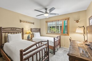 Un dormitorio con dos camas de madera, un ventilador de techo, una ventana con vistas y una decoración de cabeza de venado.