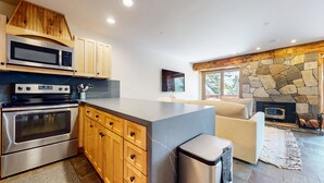 A modern kitchen with built-in appliances, wooden cabinets, a stone fireplace, and a cozy seating area. - Lakeview Villas #09 3 Bedroom Condo by RedAwning (Mammoth Lakes)