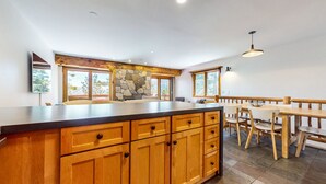 A kitchen with wooden cabinets, a stone accent wall, and a dining area with a wooden table and chairs. - Lakeview Villas #09 3 Bedroom Condo by RedAwning (Mammoth Lakes)