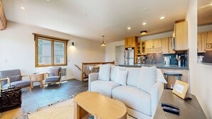 A modern living room with a sofa, a coffee table, and a dining area with a table and chairs. - Lakeview Villas #09 3 Bedroom Condo by RedAwning (Mammoth Lakes)