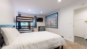 A bedroom with a bunk bed, a single bed, a dresser, a TV, and a framed picture on the wall.