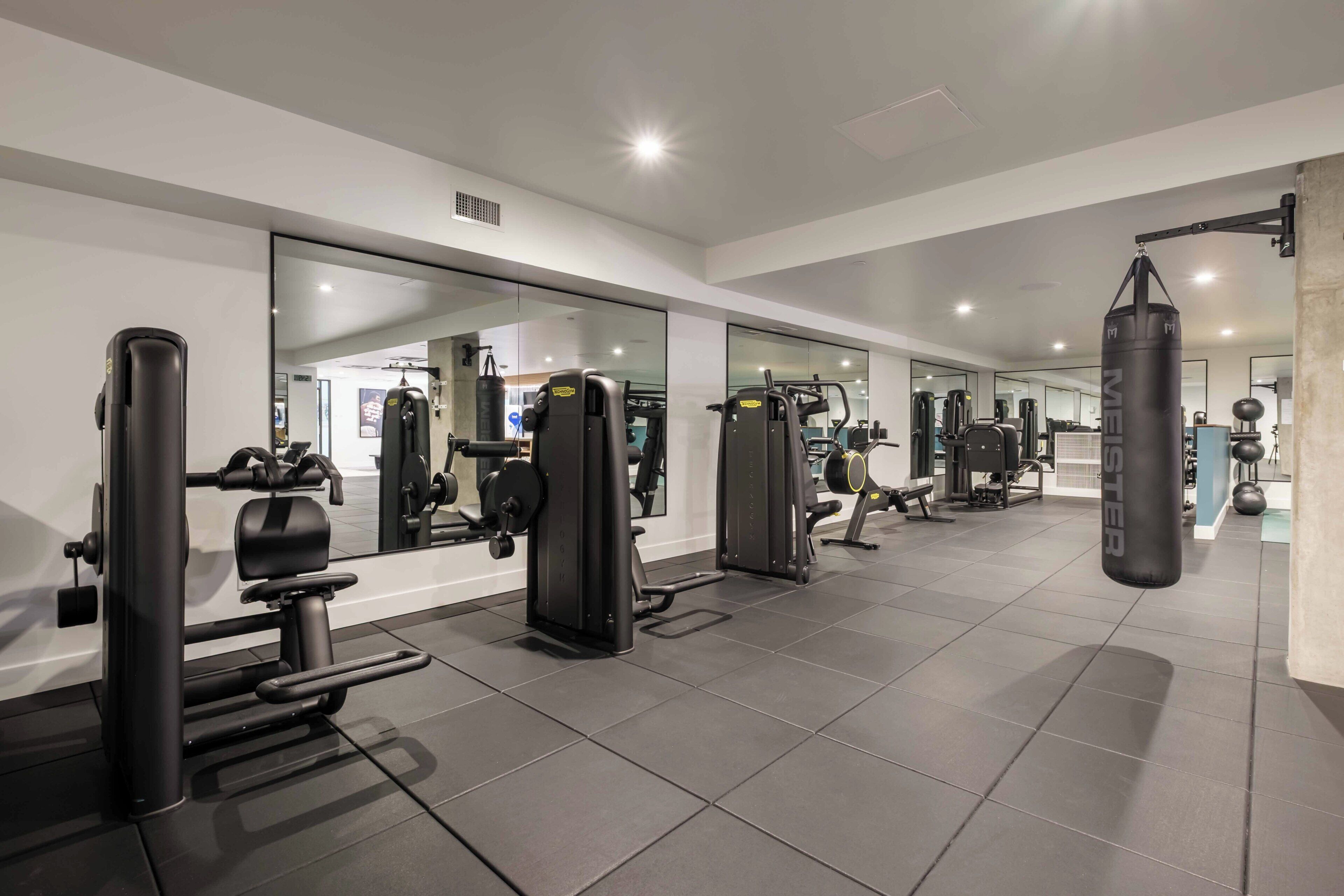 Academia moderna com diversos aparelhos de exercício, um saco de pancadas e um espelho grande refletindo os equipamentos.