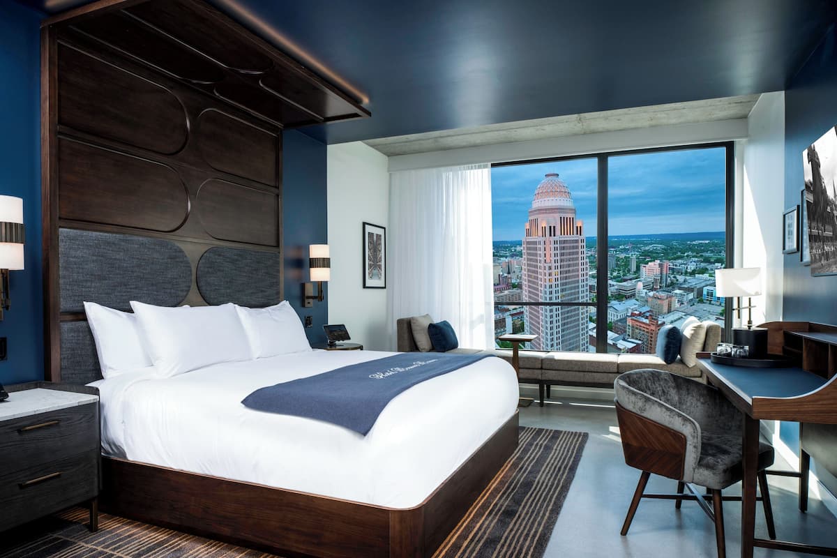 Une chambre d’hôtel moderne, dotée d’un grand lit, d’un bureau et offrant une vue sur le paysage urbain.