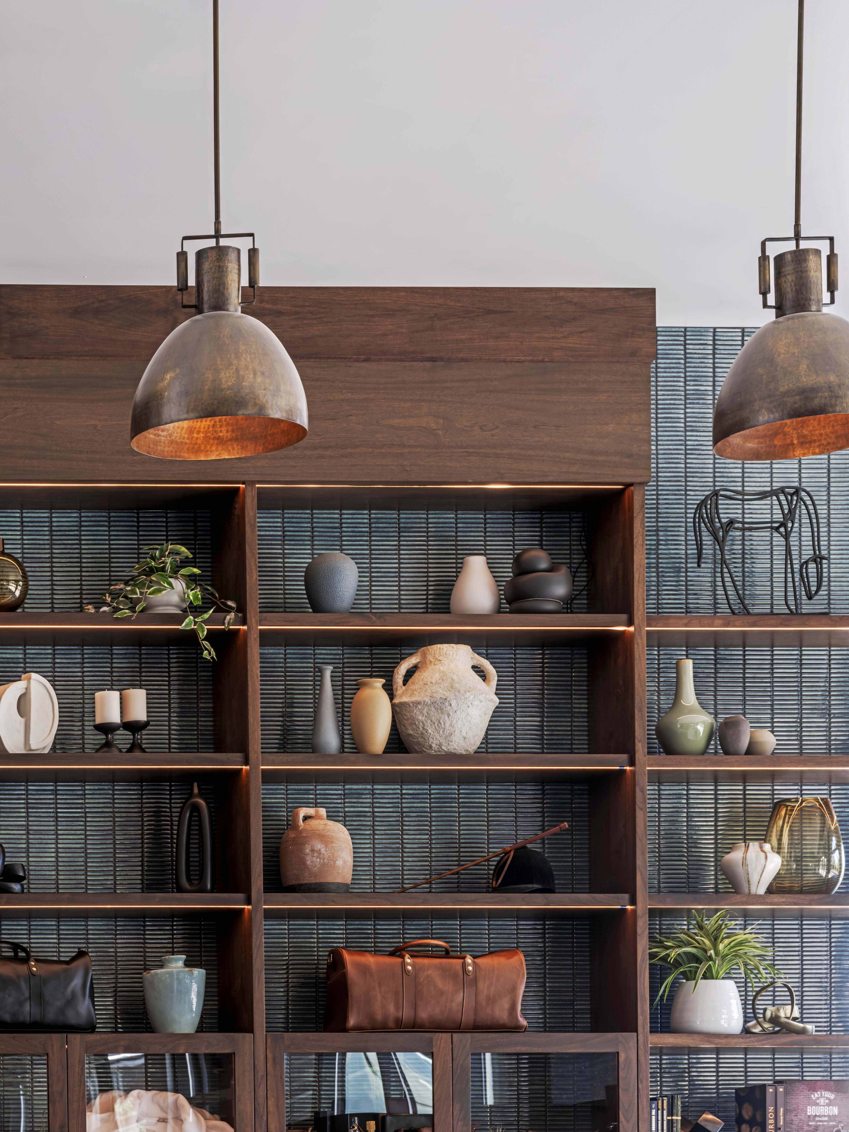 Quarto com prateleiras de madeira exibindo diversos objetos decorativos e duas luminárias pendentes em estilo industrial.