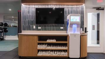 A modern hotel lobby with a large flat-screen TV, a self-service kiosk, and neatly arranged rolled towels.