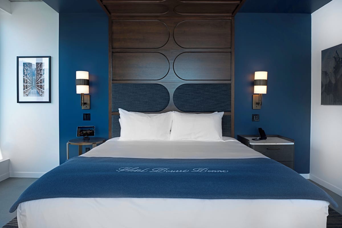 Une chambre d’hôtel avec un grand lit, deux tables de chevet, une tête de lit et des lampes fixées au mur.