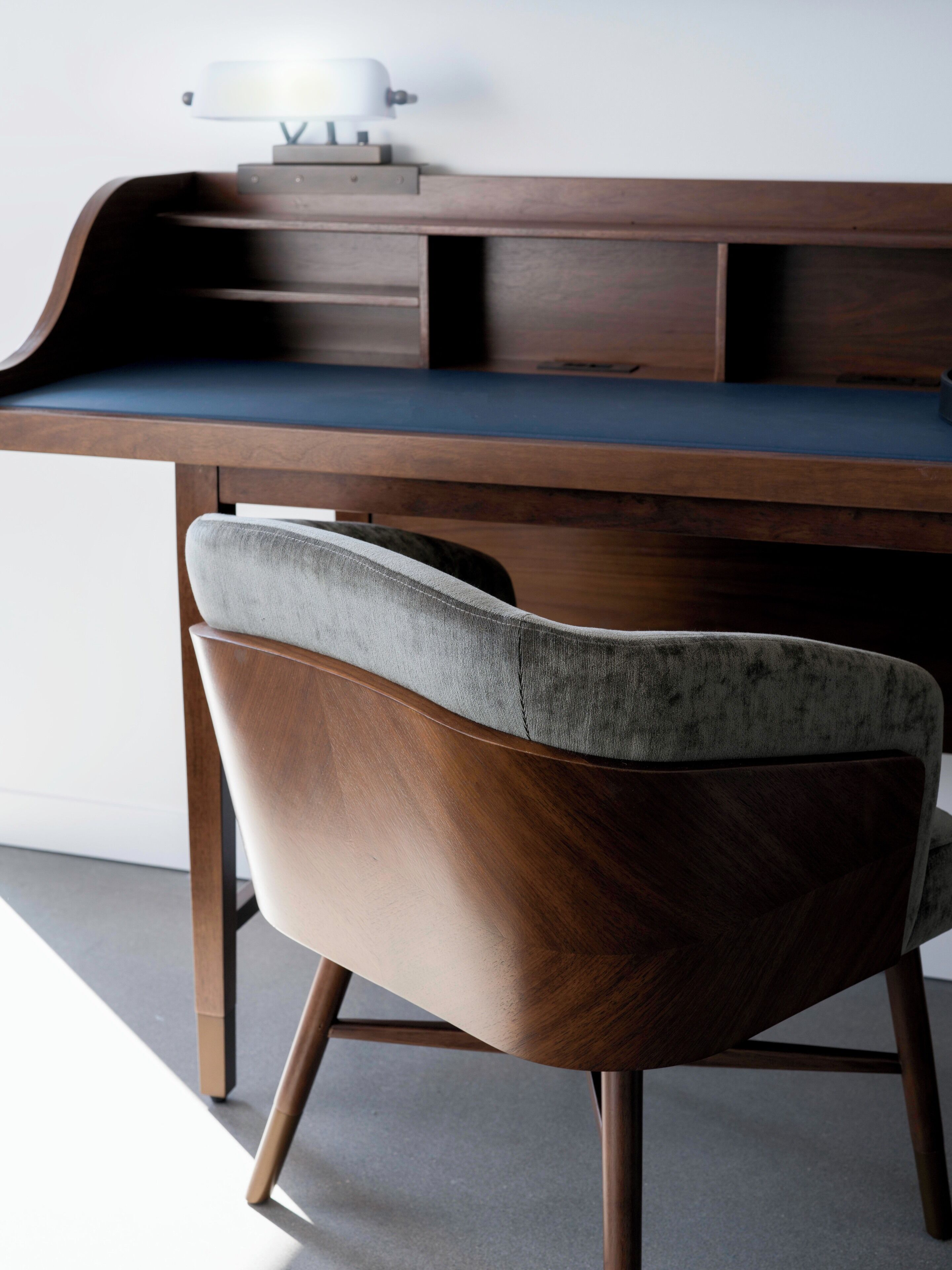 A modern desk with a curved design and a chair with a wooden frame and grey upholstery.