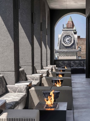 Un espacio al aire libre con sofás y mesas, una chimenea y una torre del reloj al fondo.