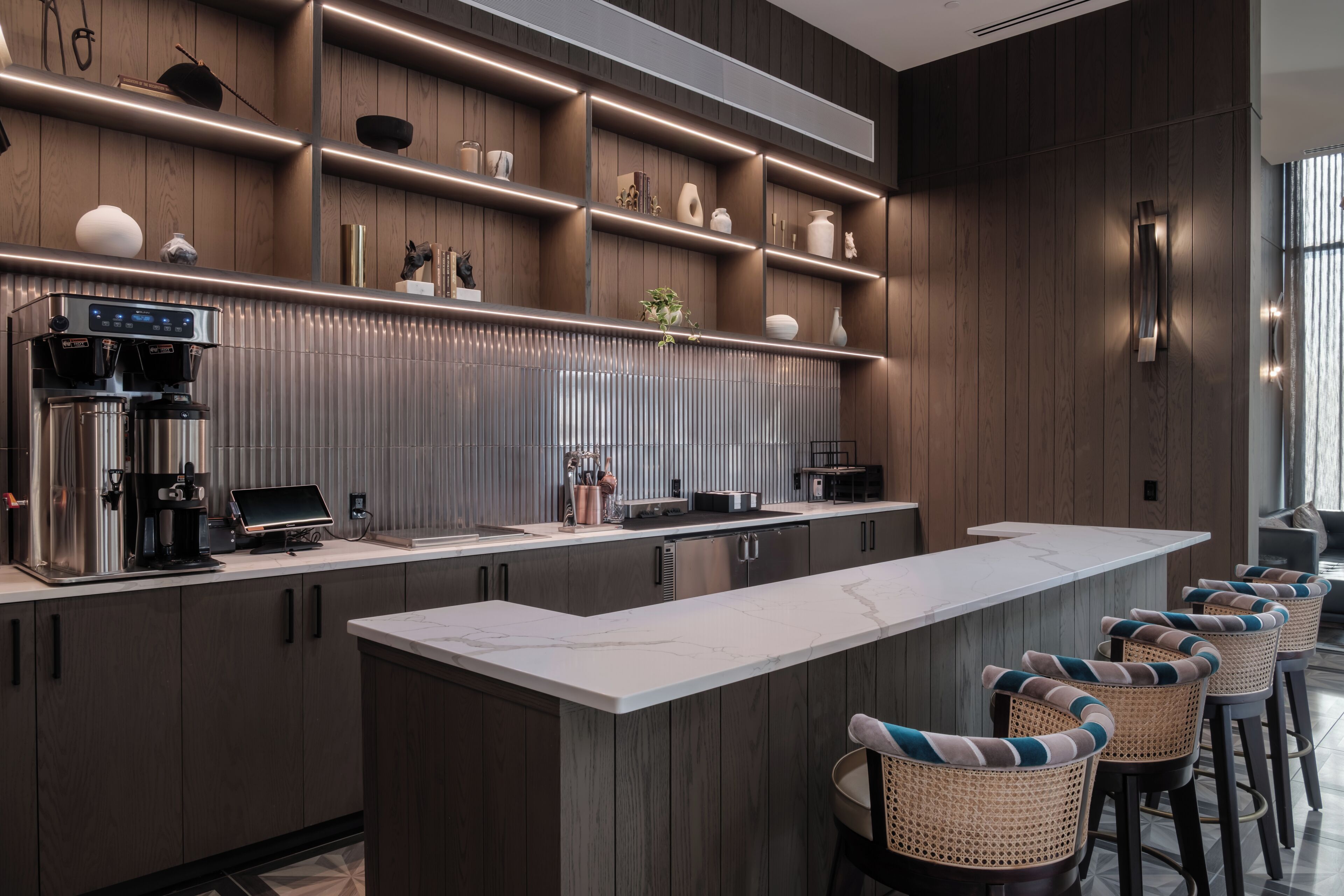 A modern kitchen with a long island, bar stools, and a coffee machine.