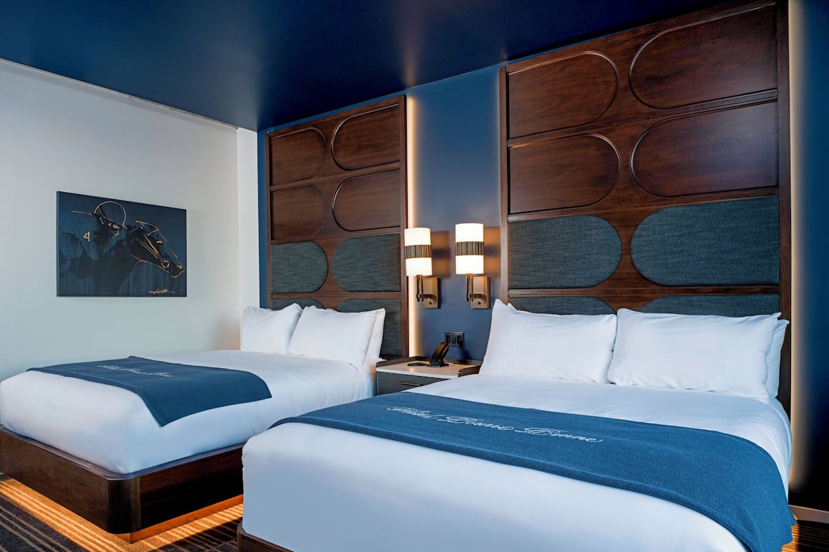 Une chambre d’hôtel avec deux lits, une grande œuvre d’art murale et une tête de lit moderne dotée d’un éclairage intégré.