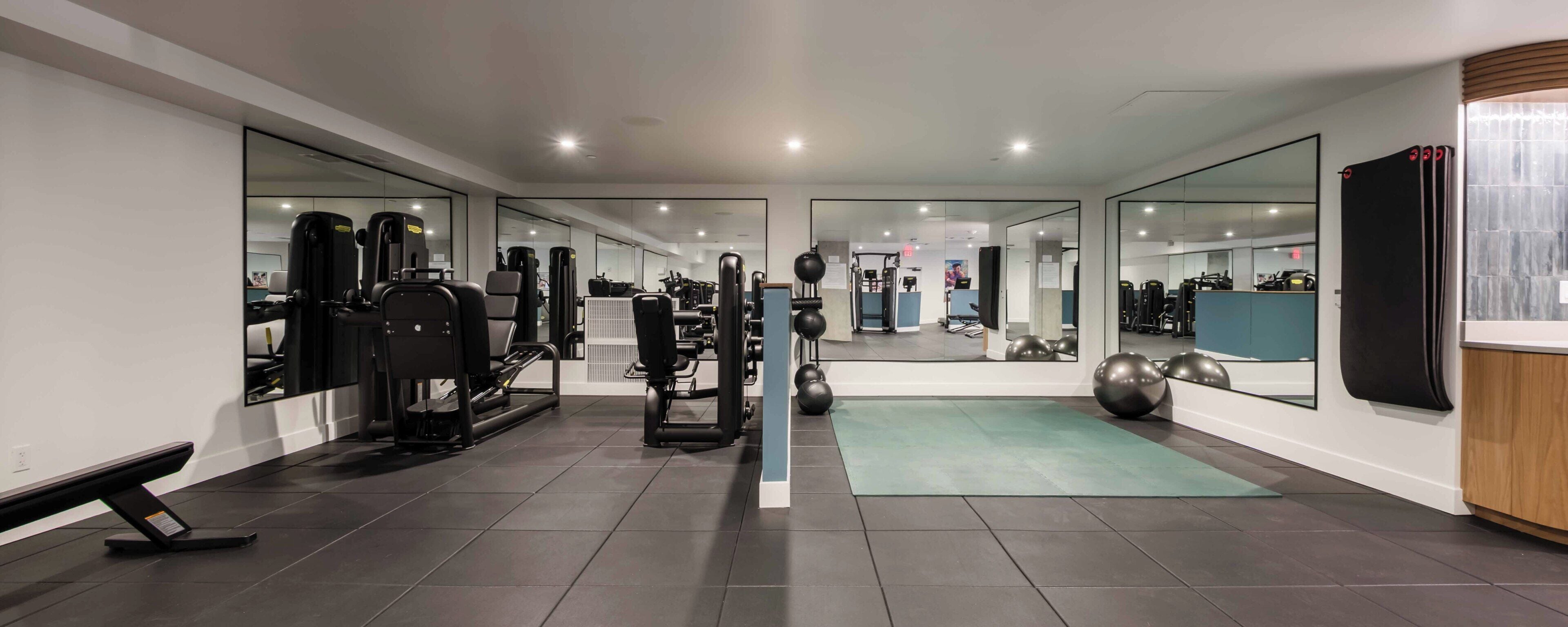 Et fitnessrum med træningsudstyr, et spejlpanel og en grøn måtte.