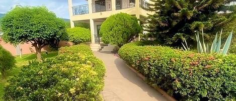 A two-story building with a balcony, surrounded by well-maintained hedges and a clear sky.