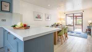 Una cocina moderna con encimera de mármol, un área de comedor con sillas verdes y vistas a través de un ventanal.