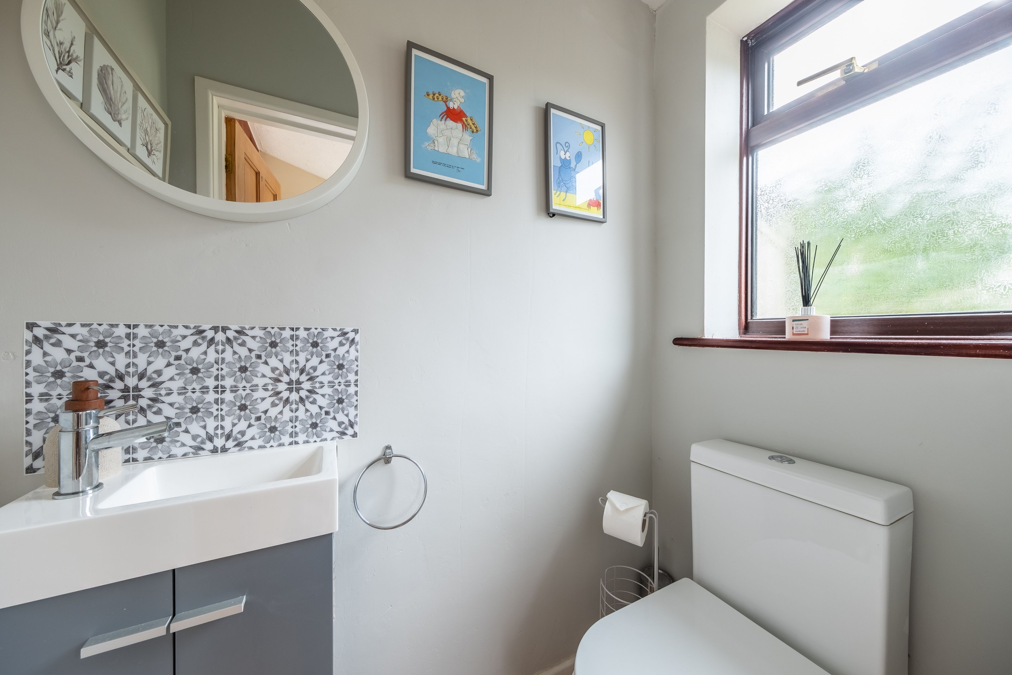 A bathroom with a white sink, a mirror, a toilet, and framed pictures on the wall.