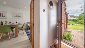Un comedor con mesa y sillas de madera, una puerta de vidrio que da al exterior y un cuadro de paisaje urbano en la pared.