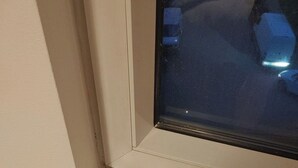 Ein Eckbereich eines Zimmers mit weißer Wand und Fenster mit schwarzem Rahmen.