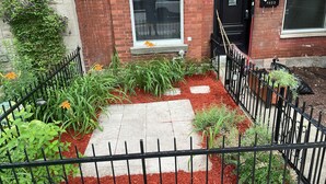 Ein Garten mit einer Backsteinmauer, einem schwarzen Metallzaun und verschiedenen Pflanzen und Blumen.