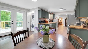 A modern kitchen with green cabinets, a dining table with a vase of flowers, and a view of the outdoors through large sliding doors.