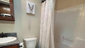 Ein Badezimmer mit einem Holzkosmetikschrank, einer Toilette, einer Duschkabine mit Vorhang und einem Bild an der Wand.