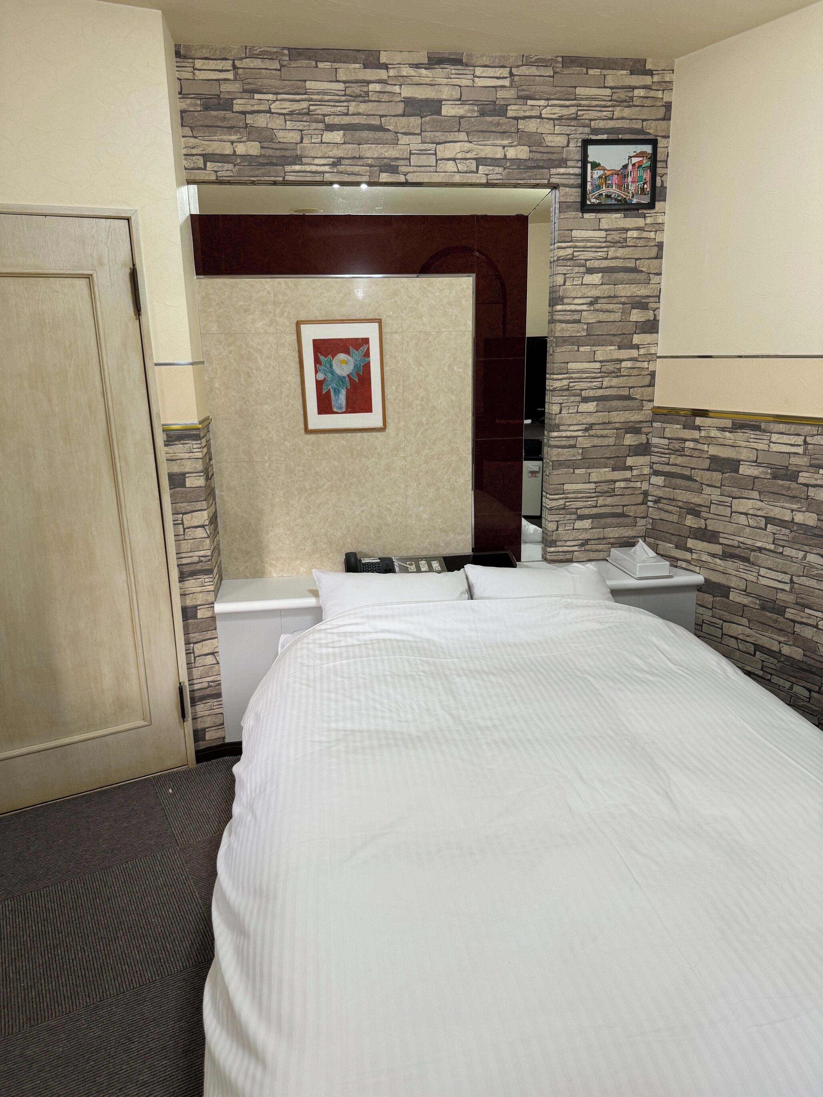 Een hotelkamer met een bed, een telefoon, een tafeltje en een foto aan de muur.