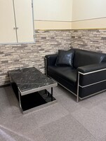 Un pequeño espacio de oficina con un sofá de cuero negro, una mesa de superficie de mármol y una pared con diseño de piedra.