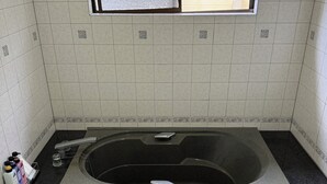 Et badeværelse med badekar, et vindue og en flisebeklædt væg.